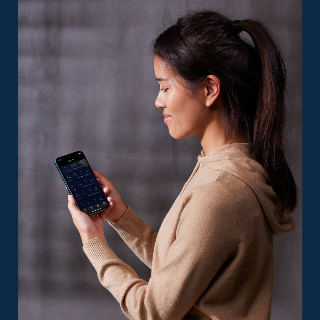 A woman is smiling while looking at the OxyKnight Watch app on her smartphone