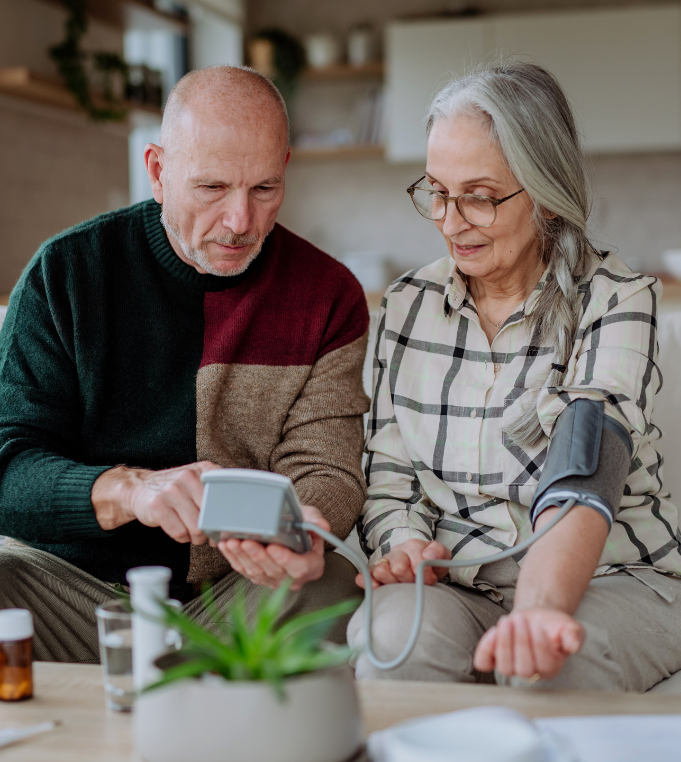 A senior citizen or older couple help each other take their blood pressure at home