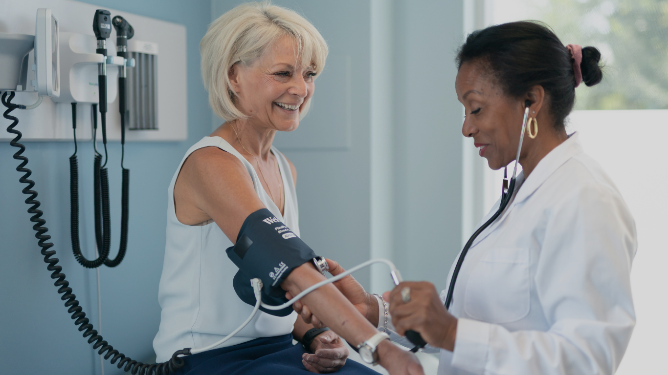 A older woman smiles at her doctor while her doctor takes her blood pressure