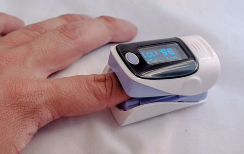 A person's hand with a pulse oximeter attached to the index finger.