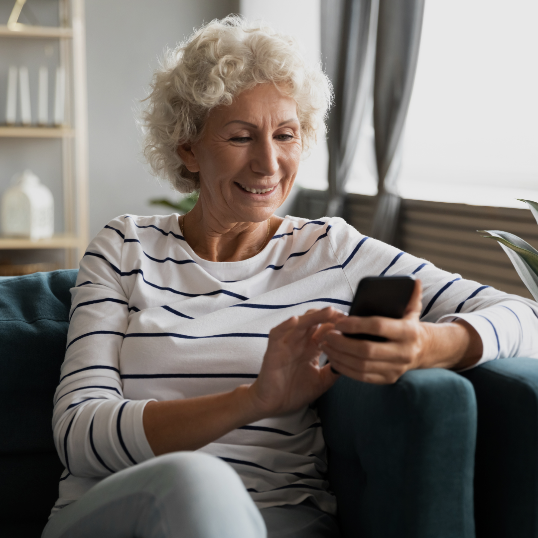 An older woman is smiling while checking her smart phone