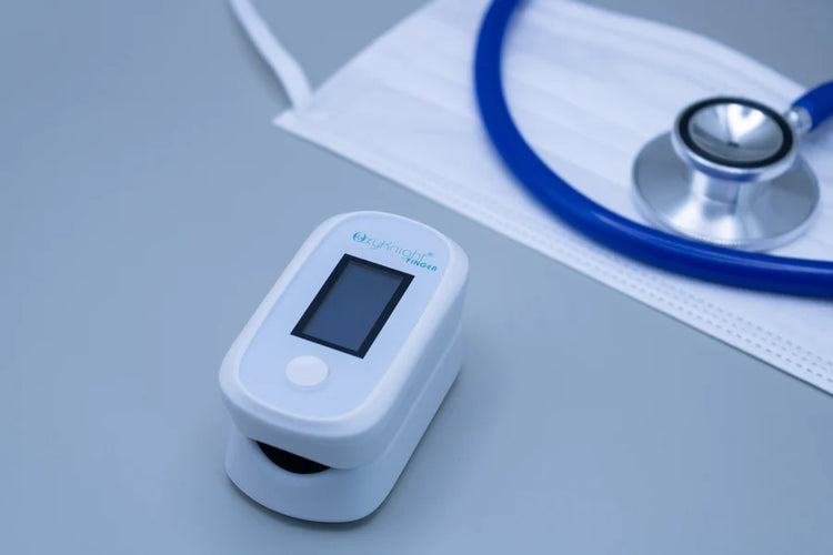 CMI Health OxyKnight® Fingertip Pulse Oximeter placed on a table beside a stethoscope and face mask.