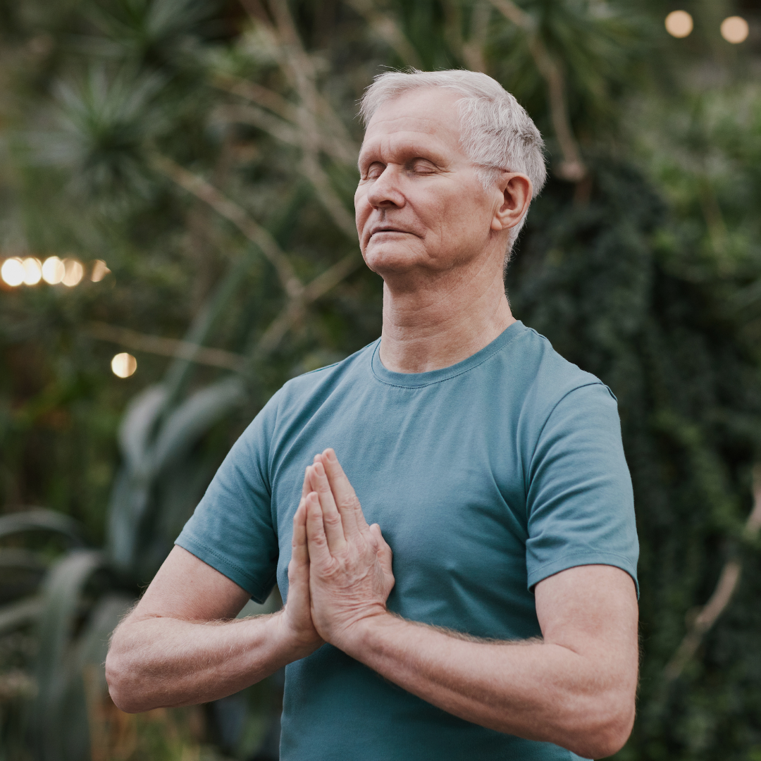 A older gentleman or senior is shown posing in his yoga class